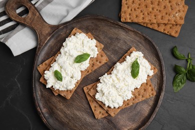 Photo of Crispy crackers with cottage cheese and basil on black table, flat lay