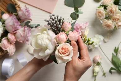 Florist creating beautiful bouquet at white table, top view