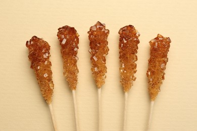 Photo of Wooden sticks with sugar crystals on beige background, flat lay. Tasty rock candies