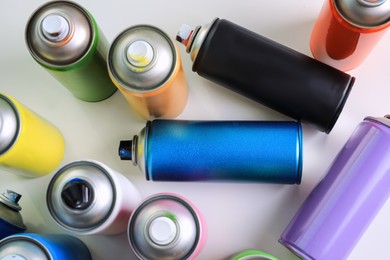 Cans of different graffiti spray paints on white table, flat lay