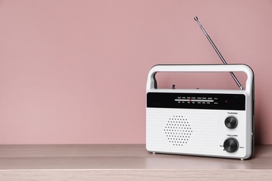 Retro radio receiver on wooden table against pink background. Space for text