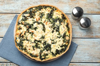 Photo of Delicious homemade spinach quiche with salt and pepper shakers on rustic wooden table, flat lay