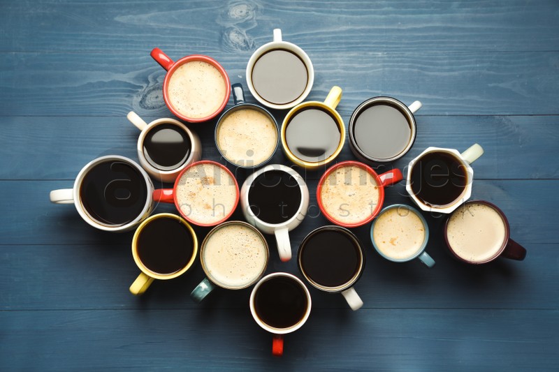 Photo of Many cups of different coffee drinks on blue wooden table, flat lay