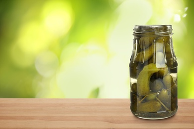 Jar of pickled cucumbers on wooden table against blurred background, space for text 