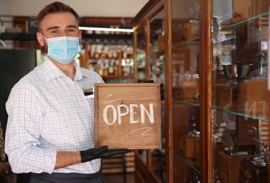 Waiter holding OPEN sign in restaurant. Catering during coronavirus quarantine