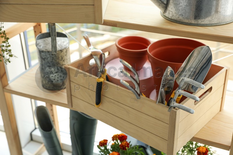 Photo of Wooden crate with gardening tools on rack indoors