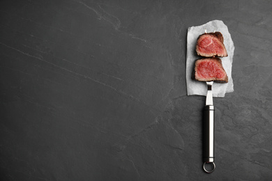 Carving fork with slices of delicious beef tenderloin on black table, top view. Space for text