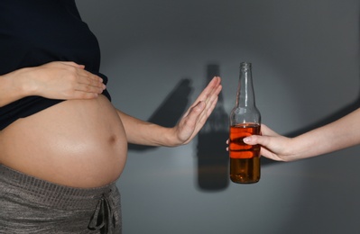 Pregnant woman declining whiskey on dark background. Alcohol harm