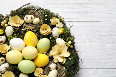Decorative wreath with Easter eggs on white wooden background, top view