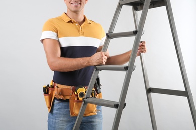 Professional builder with metal ladder on grey background, closeup