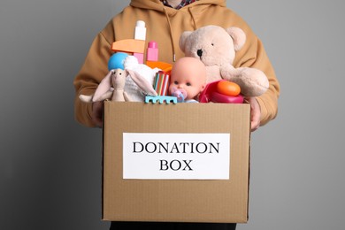 Man holding donation box full of different toys on grey background, closeup