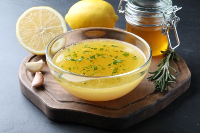 Photo of Bowl with lemon sauce and ingredients on dark table. Delicious salad dressing