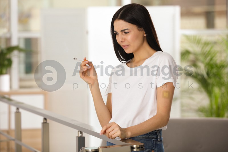Photo of Emotional young woman with nicotine patch and cigarette indoors