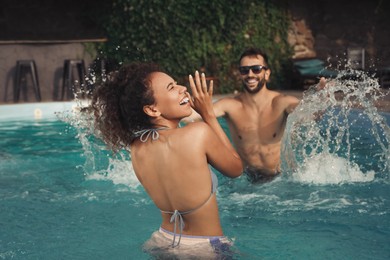 Happy couple having fun in outdoor swimming pool on sunny summer day