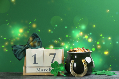 Composition with pot of gold coins and wooden block calendar on grey stone table against green background. St. Patrick's Day celebration