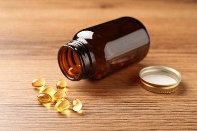 Photo of Overturned bottle with dietary supplement capsules on wooden table