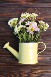 Photo of Watering can with flowers on wooden table, top view