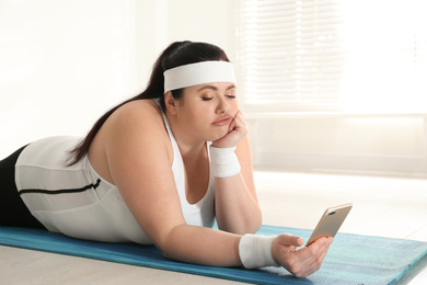 Lazy overweight woman using mobile phone instead of training at gym