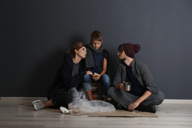 Poor homeless family sitting on floor near dark wall