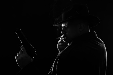 Old fashioned detective with gun smoking cigarette on dark background, black and white effect