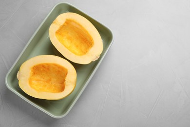Raw spaghetti squash halves in baking dish on light table, top view. Space for text