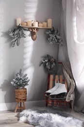 Pair of ice skates, sleigh and beautiful Christmas decor near white wall indoors