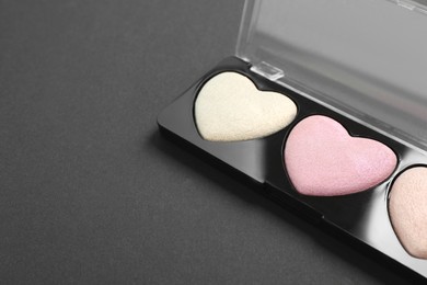 Photo of Palette of heart shaped eyeshadows on dark background, closeup. Space for text