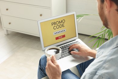 Man holding laptop with activated promo code and cup of coffee indoors, closeup