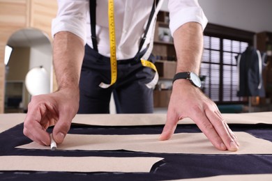 Photo of Professional tailor marking sewing pattern on fabric with chalk at table in workshop, closeup