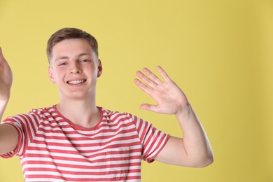 Happy teenage boy taking selfie on yellow background