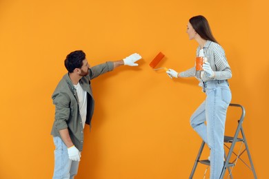 Photo of Man and woman painting orange wall. Interior design
