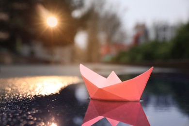 Pink paper boat in puddle on street