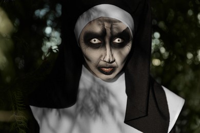 Photo of Portrait of scary devilish nun near tree outdoors. Halloween party look