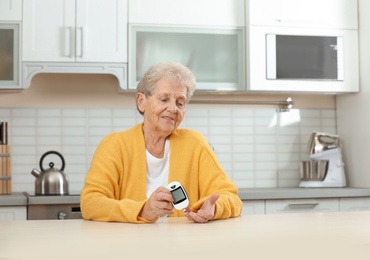 Senior woman using digital glucometer at home. Diabetes control
