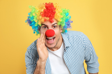 Funny man with clown nose and rainbow wig on yellow background. April fool's day