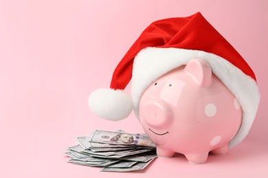 Piggy bank with Santa hat and dollar banknotes on pink background. Space for text