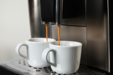 Espresso machine pouring coffee into cups against light background, closeup