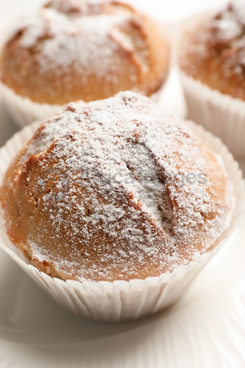 Tasty muffins powdered with sugar on plate, closeup