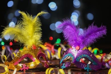Beautiful carnival masks and party decor on table against blurred lights