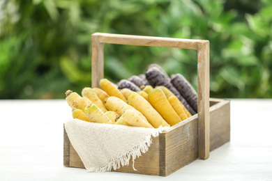 Different raw carrots in wooden basket on white table against blurred background