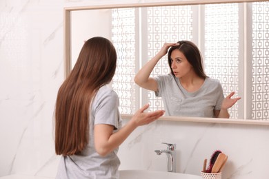 Young woman with hair loss problem looking near mirror in bathroom