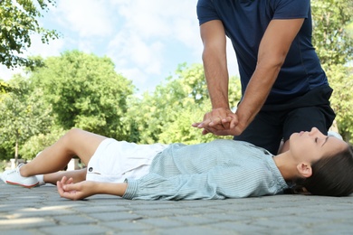 Man performing CPR on unconscious young woman outdoors. First aid