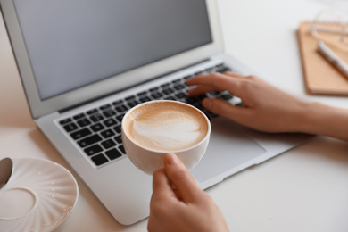 Young blogger with cup of coffee working at table in cafe, closeup
