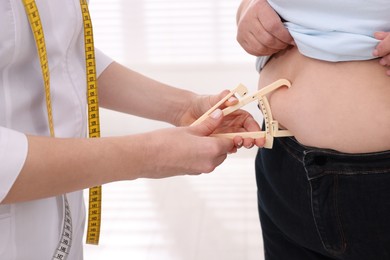 Nutritionist measuring overweight woman's body fat layer with caliper in clinic, closeup