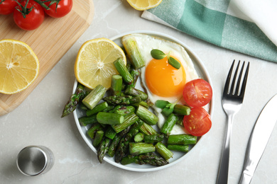 Oven baked asparagus served with fried egg on light grey marble table, flat lay