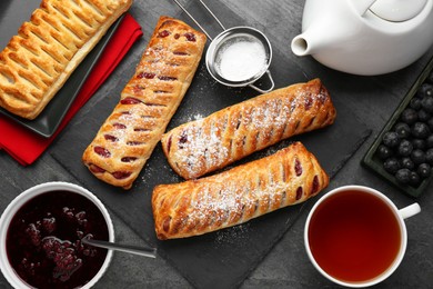 Photo of Fresh tasty puff pastry with sugar powder and tea served on grey table, flat lay
