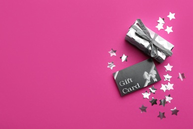 Gift card, present and confetti on pink background, flat lay. Space for text