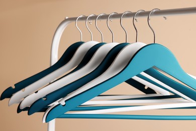 Photo of Clothes hangers on metal rail against beige background, closeup view
