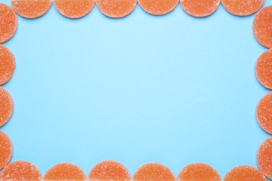 Frame made with orange marmalade candies on light blue background, flat lay. Space for text