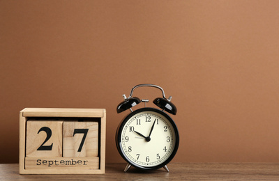 Wooden block calendar and alarm clock on table against brown background